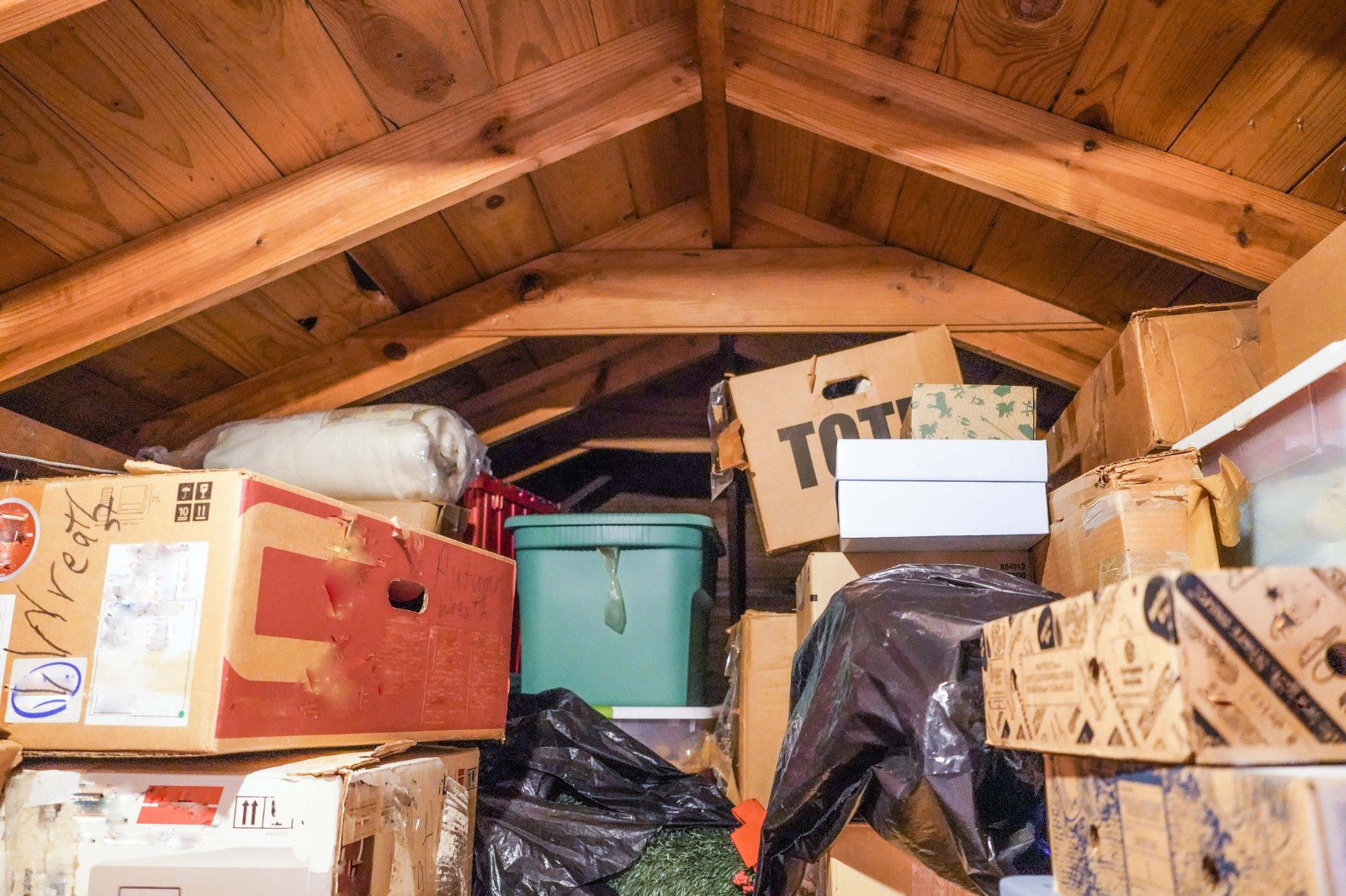 Uninsulated attic cluttered with storage bins and carboard boxes